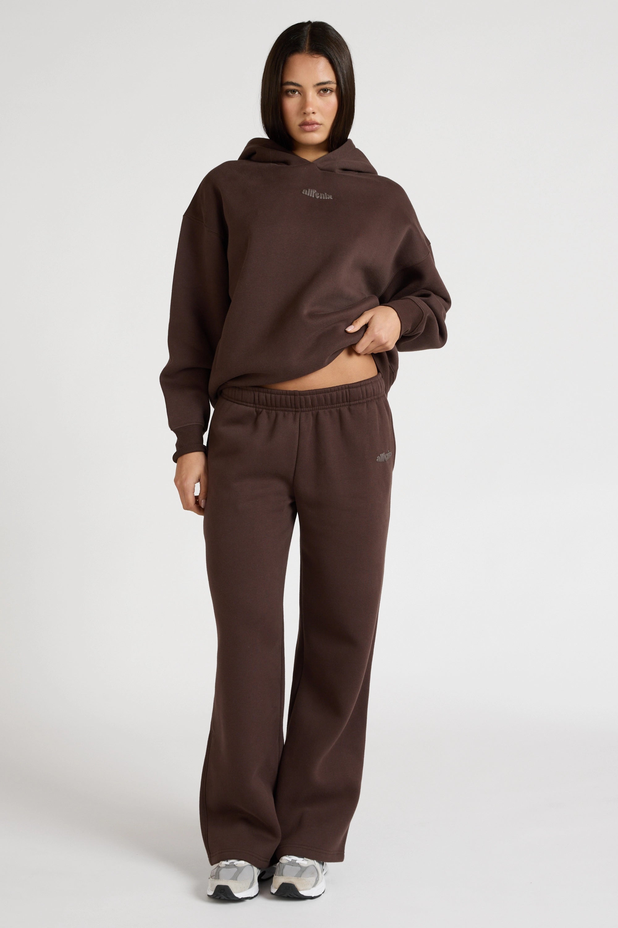 Woman wearing espresso brown hoodie and wide leg trackpants on a white background