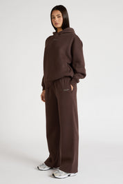 Woman wearing espresso brown hoodie and wide leg trackpants on a white background