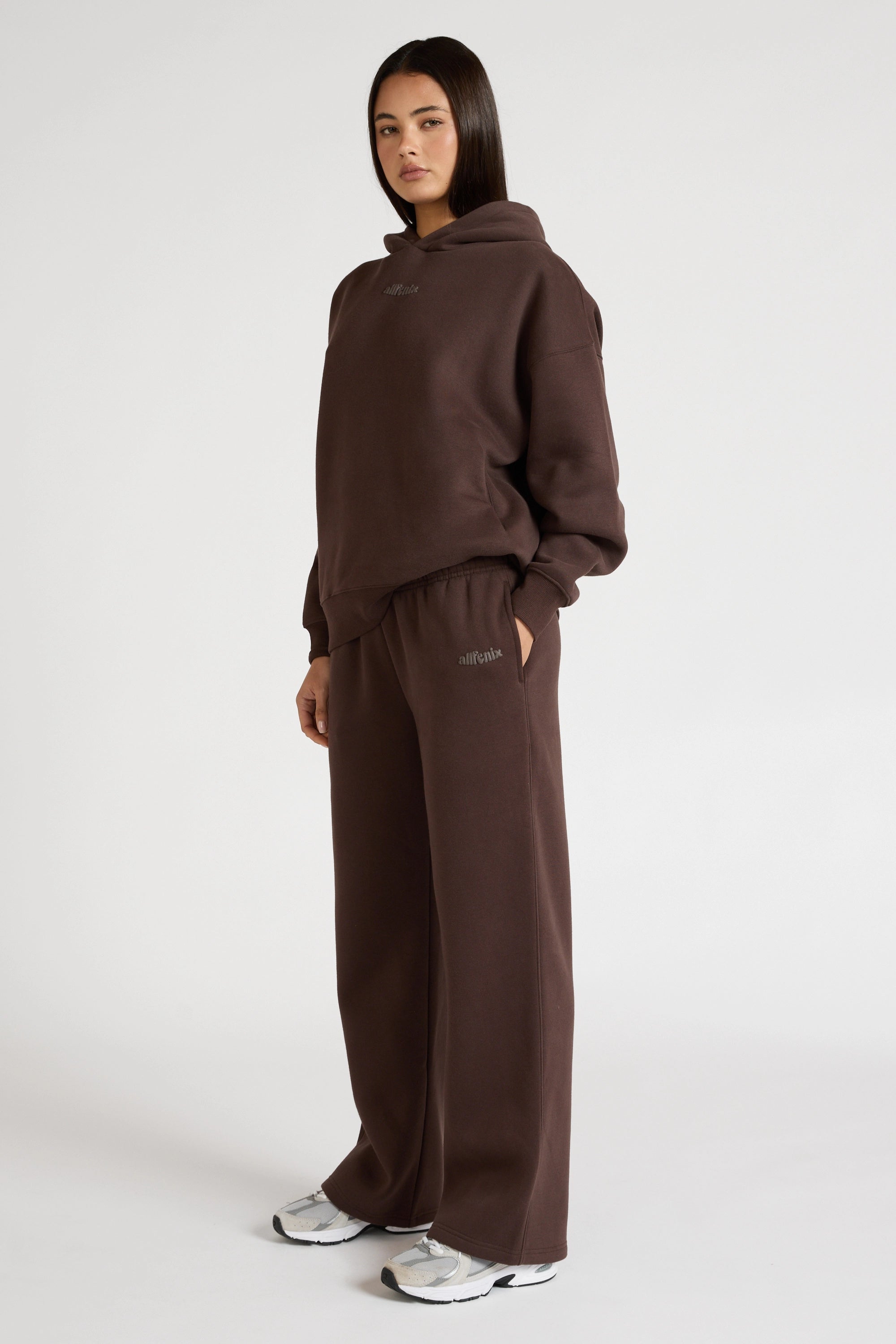 Woman wearing espresso brown hoodie and wide leg trackpants on a white background