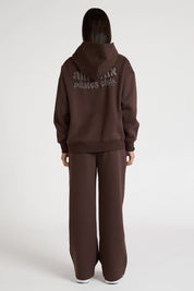 Woman wearing espresso brown hoodie and wide leg trackpants on a white background