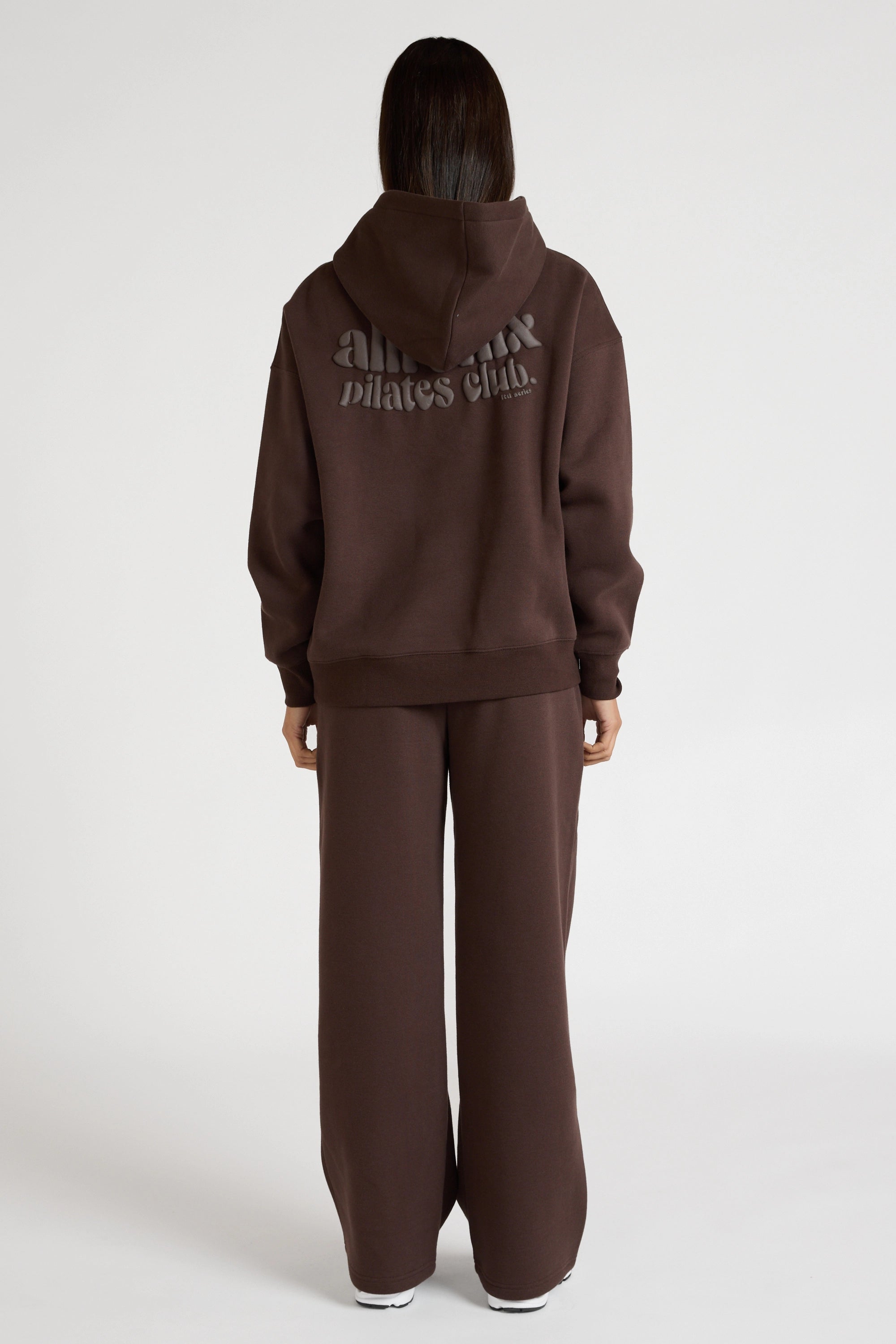 Woman wearing espresso brown hoodie and wide leg trackpants on a white background