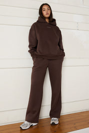 Woman wearing espresso brown hoodie and wide leg trackpants on a white background