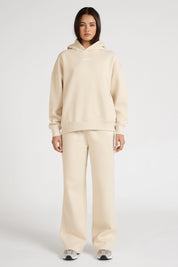Person wearing a beige hoodie and pants set on a white background