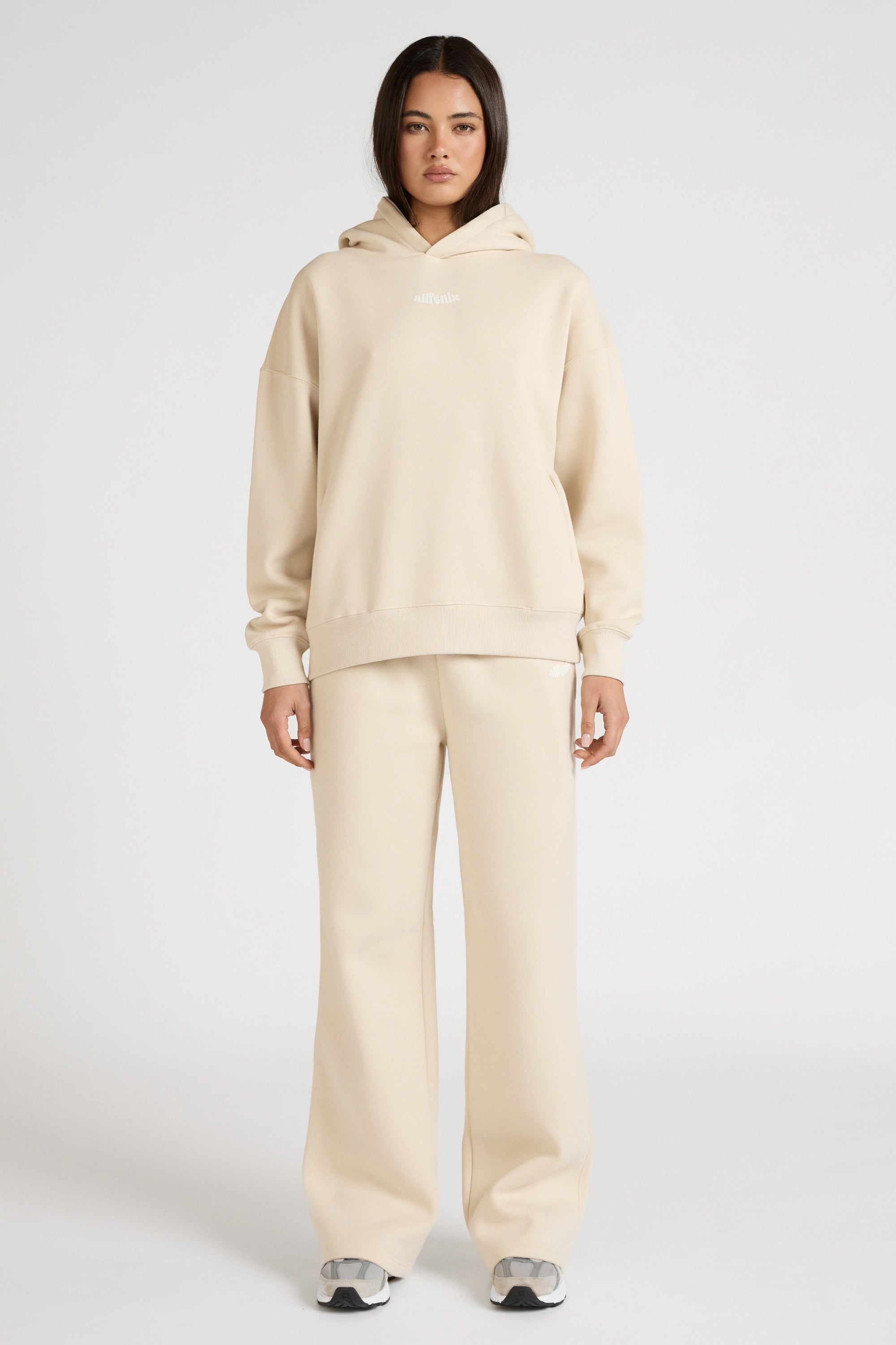 Person wearing a beige hoodie and pants set on a white background