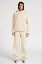 Woman wearing a clay beige hoodie and wide leg track pants on a white background