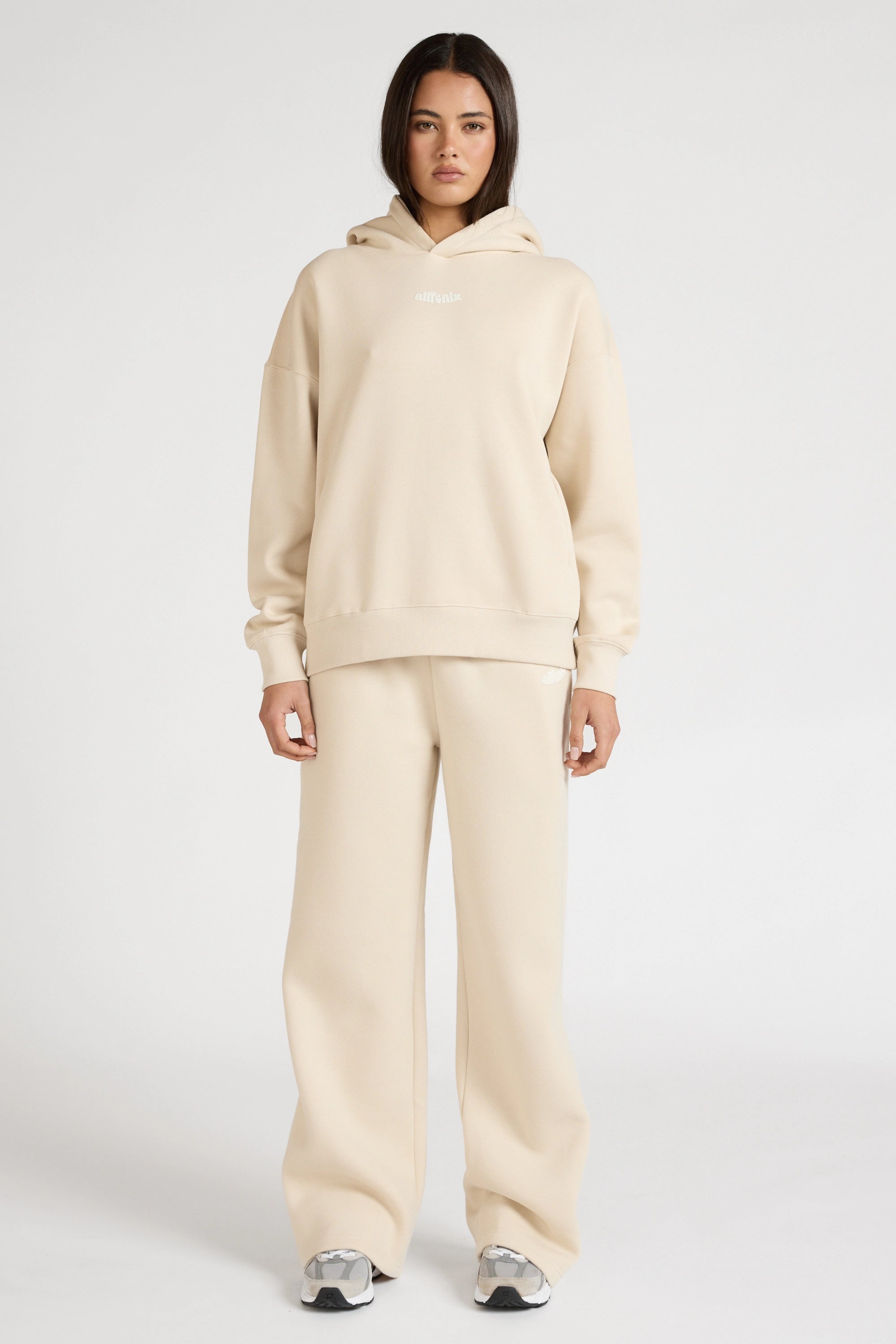 Woman wearing a clay beige hoodie and wide leg track pants on a white background