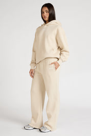 Woman wearing a clay beige hoodie and wide leg track pants on a white background