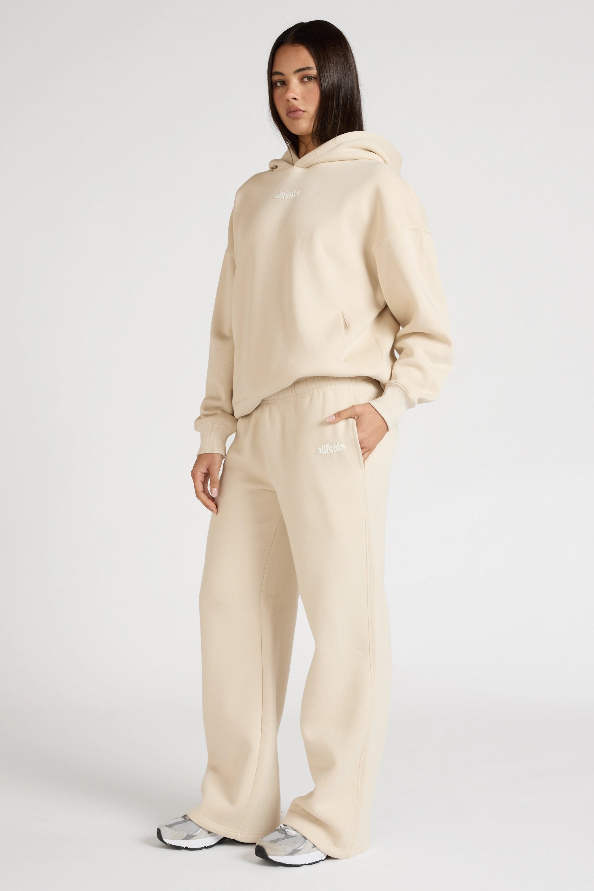 Woman wearing a clay beige hoodie and wide leg track pants on a white background