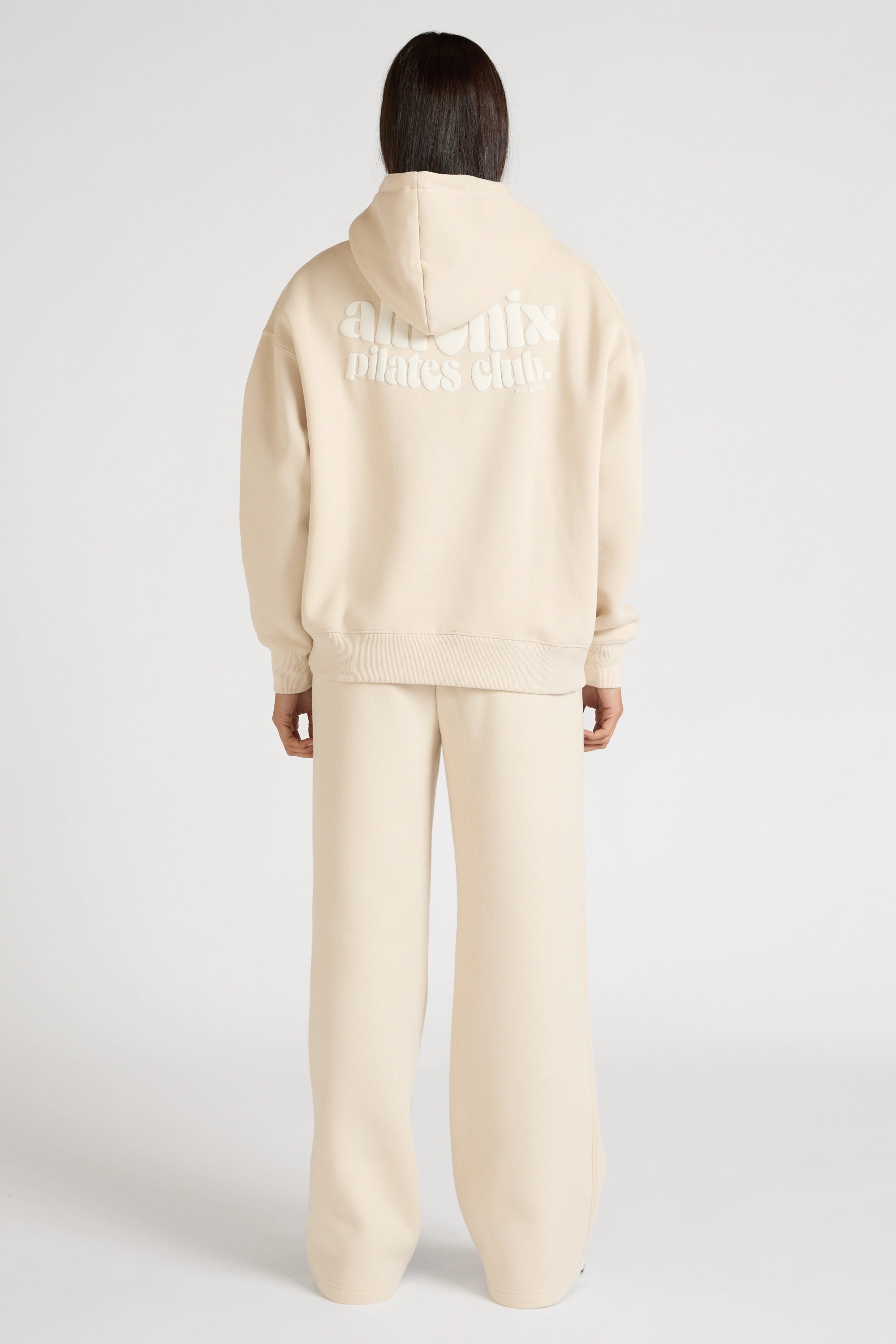 Woman wearing a clay beige hoodie and wide leg track pants on a white background