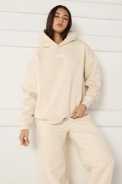 Woman wearing a beige hoodie and pants against a white background