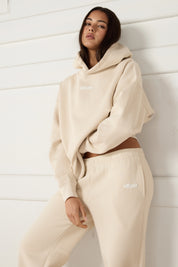 Woman wearing a beige hoodie and pants with a logo against a white background