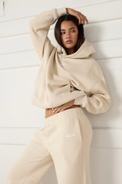 Woman wearing a beige hoodie and pants with a brand logo against a white background