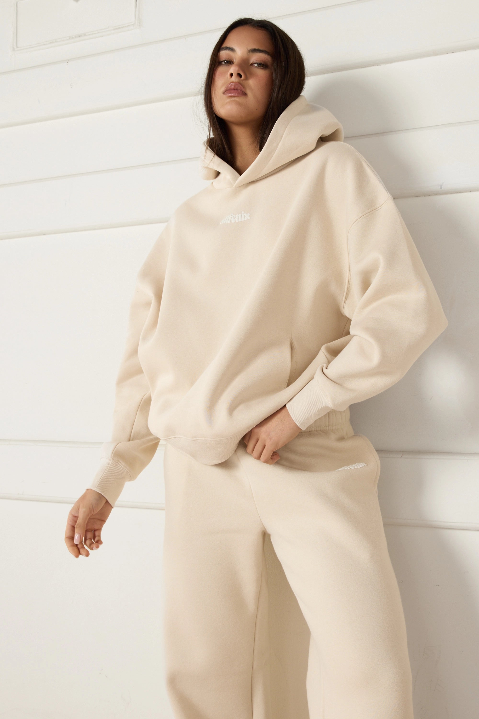 Person wearing a beige hoodie and pants against a white wall