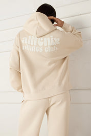 Women wearing a beige hoodie with 'allfenix unites club' text on the back against a white wall.