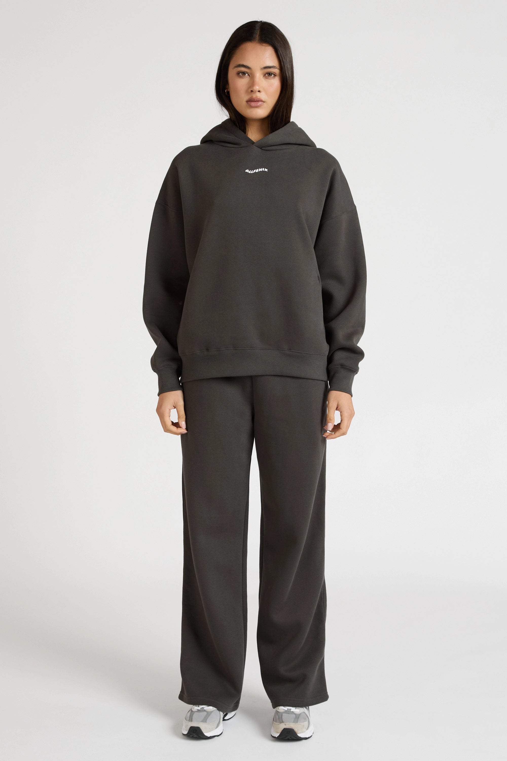 Woman wearing a dark grey hoodie and pants on a white background