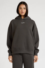 Woman wearing a dark grey hoodie with a brand logo on a white background