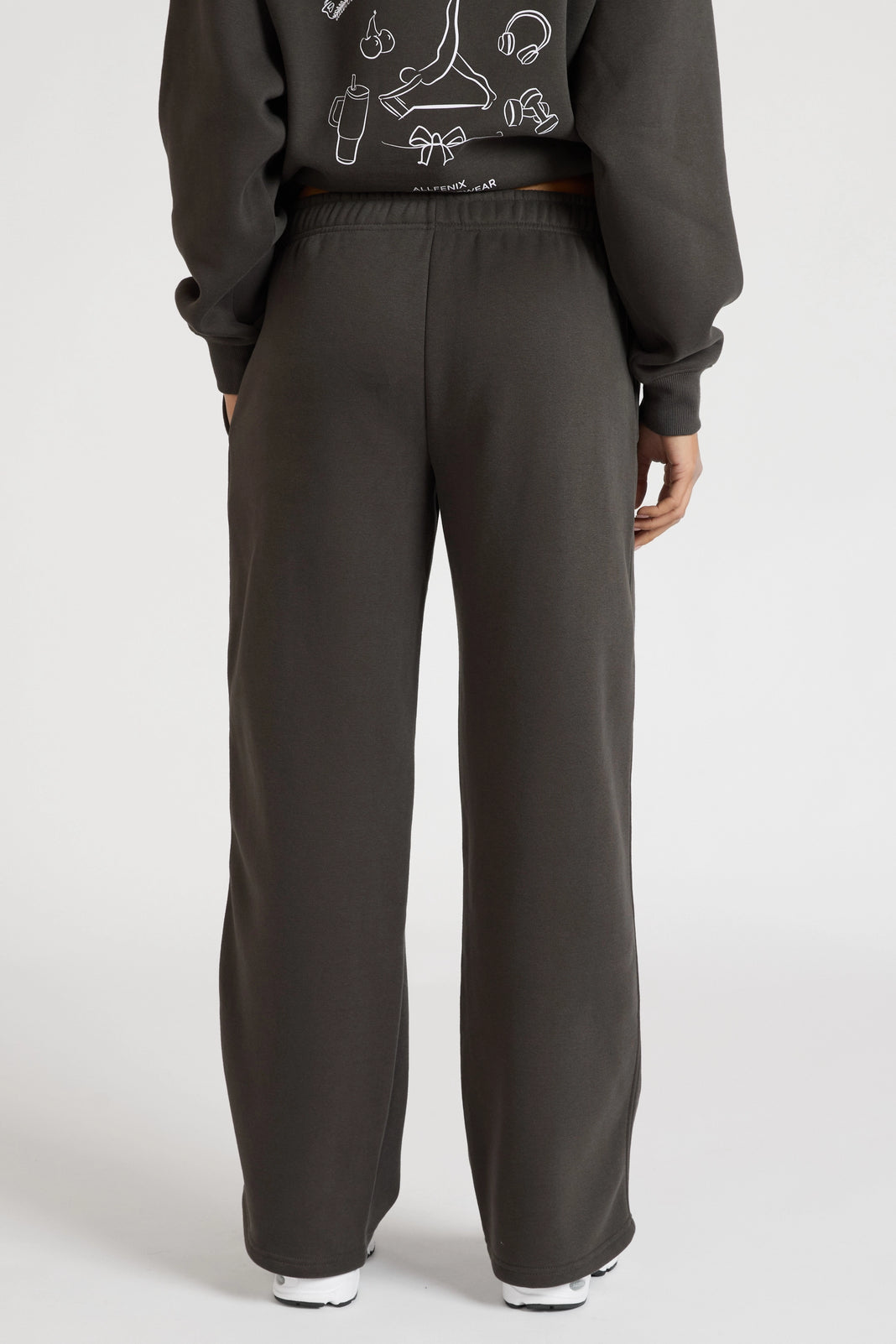 Woman wearing dark grey sweatpants and a matching hoodie on a white background