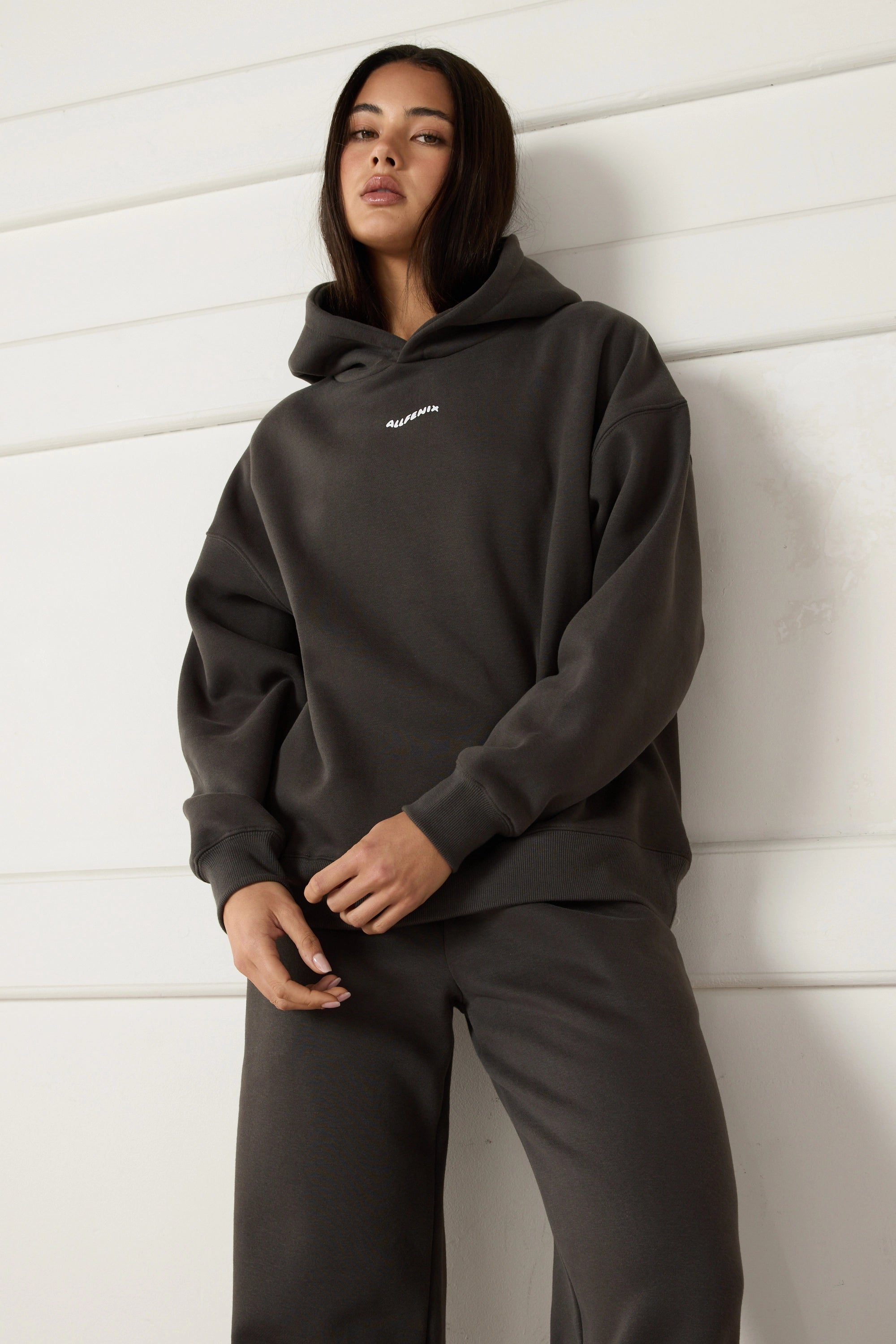 Woman wearing a dark grey hoodie with a brand logo against a light background