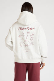 Woman wearing a white hoodie with 'Pilates Series' design on the back, standing against a white background.