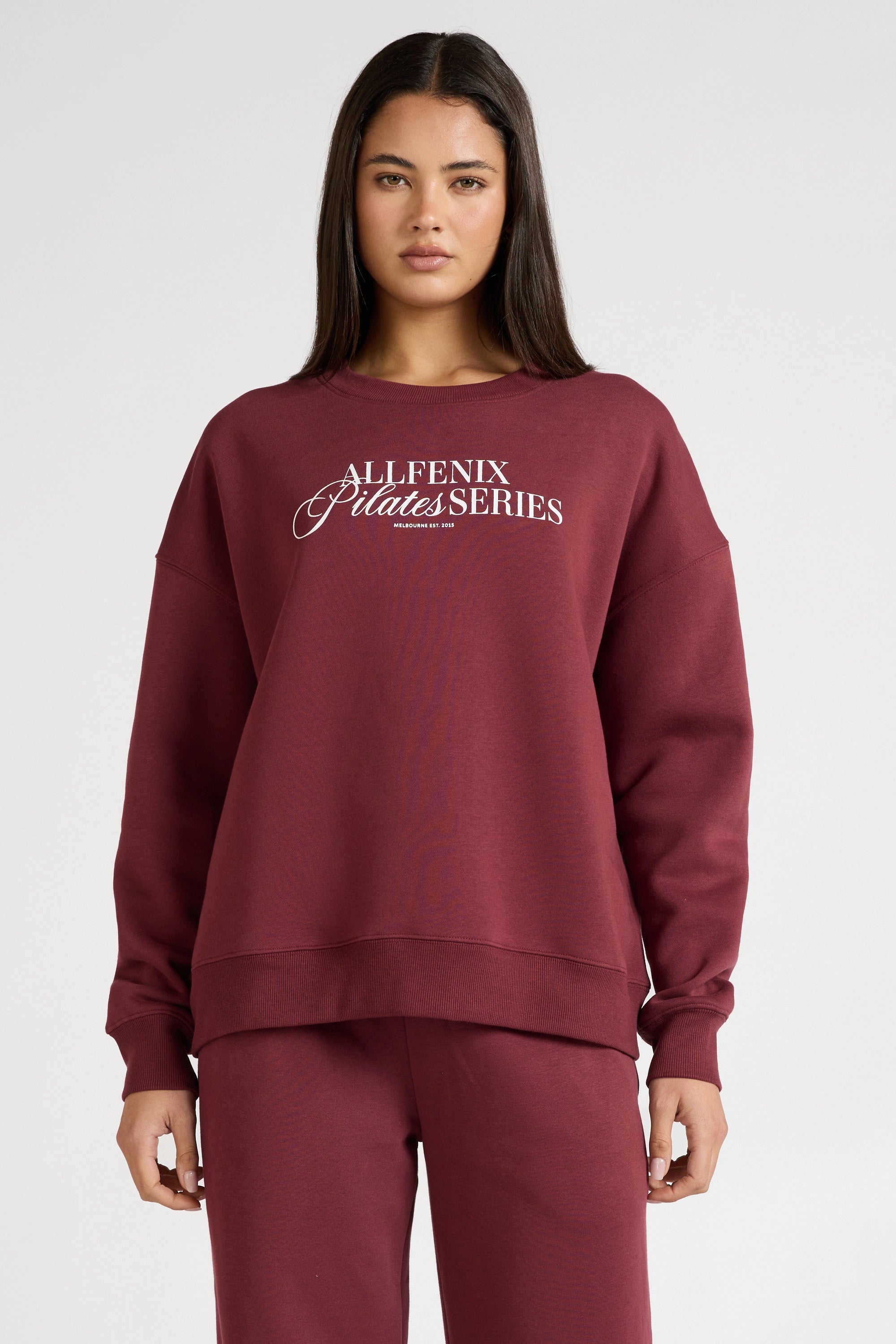 Woman wearing a maroon sweatshirt with 'All Fenix Pilates Series' text on a white background
