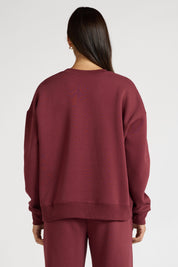 Woman wearing a maroon sweatshirt with 'All Fenix Pilates Series' text on a white background