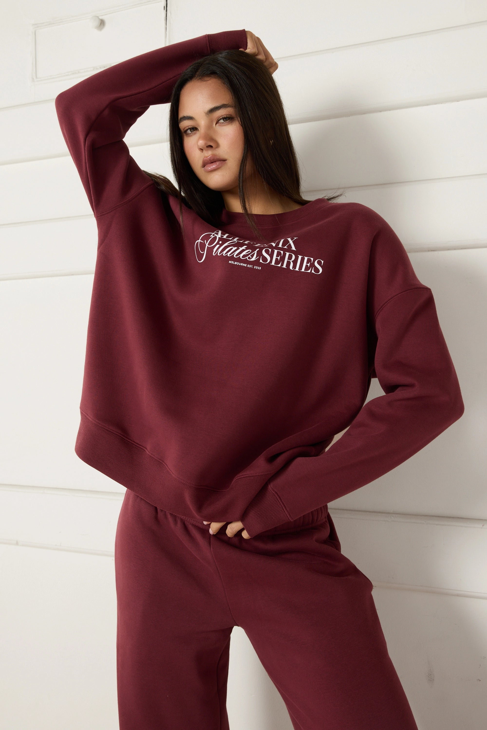 Woman wearing a maroon sweatshirt with 'All Fenix Pilates Series' text on a white background