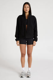 Woman wearing a black soft fleece zip jacket and bike shorts on a white background