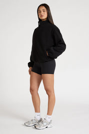 Woman wearing a black soft fleece zip jacket and bike shorts on a white background