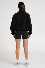 Woman wearing a black soft fleece zip jacket and bike shorts on a white background