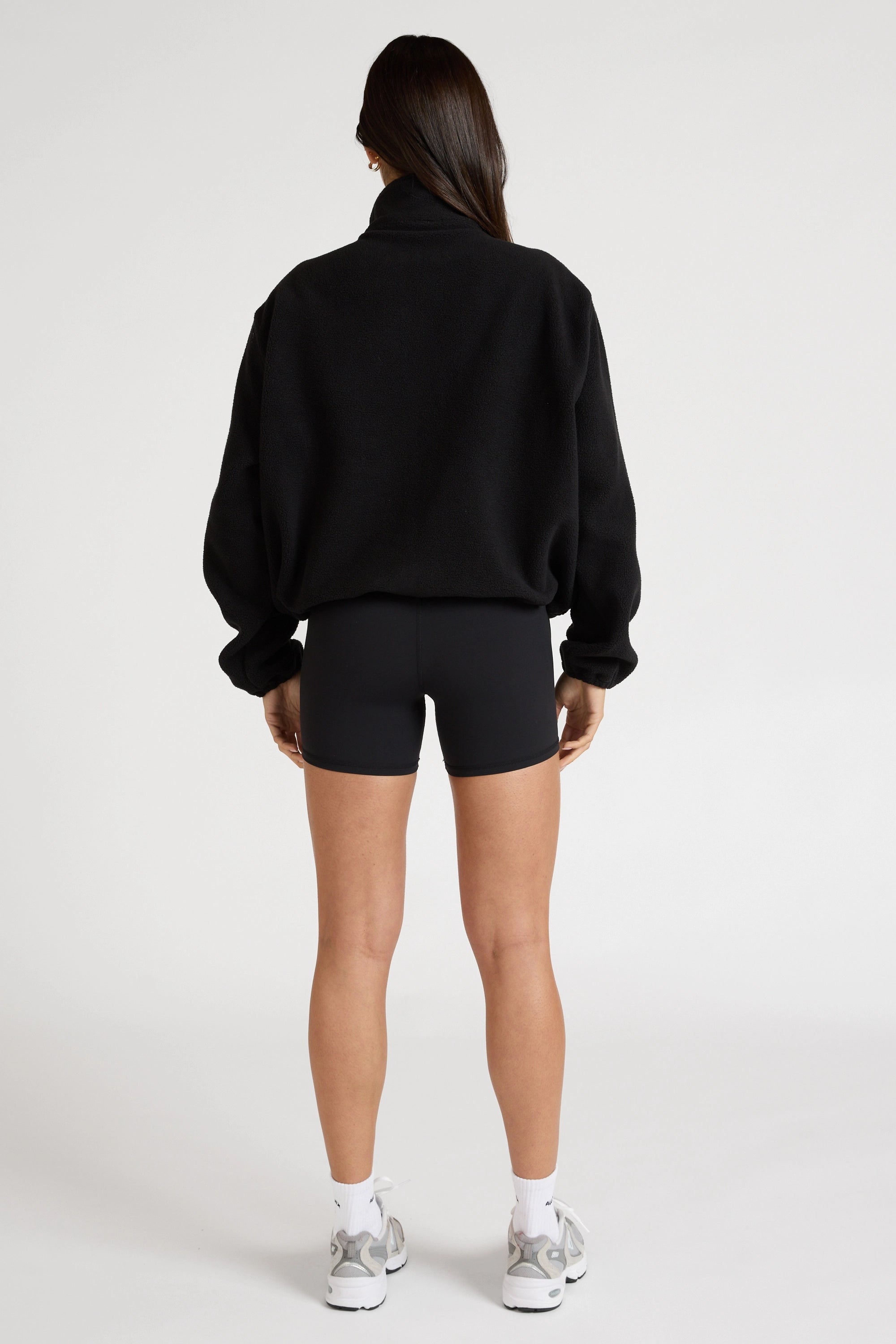 Woman wearing a black soft fleece zip jacket and bike shorts on a white background