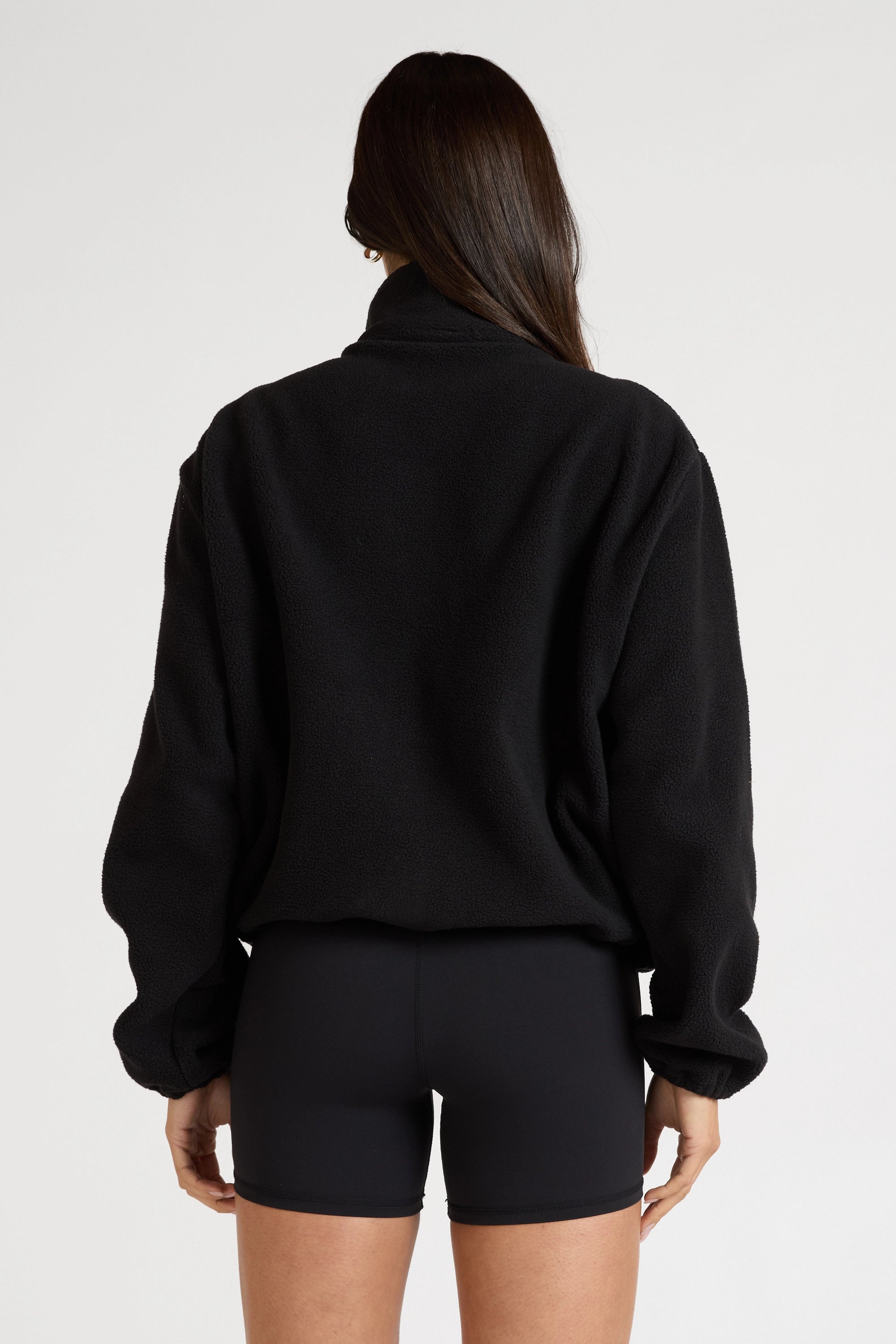 Woman wearing a black soft fleece zip jacket and bike shorts on a white background