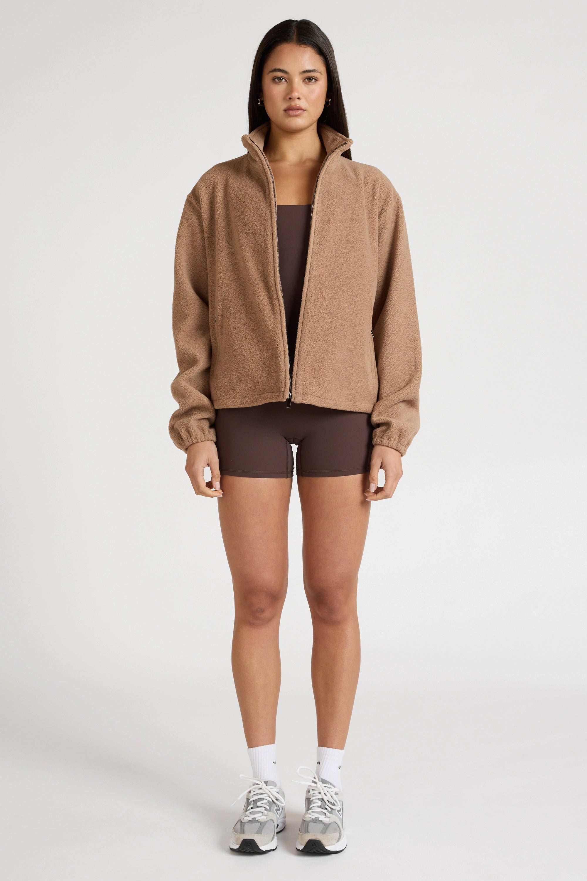 Woman wearing a brown soft fleece zip jacket and shorts on a white background