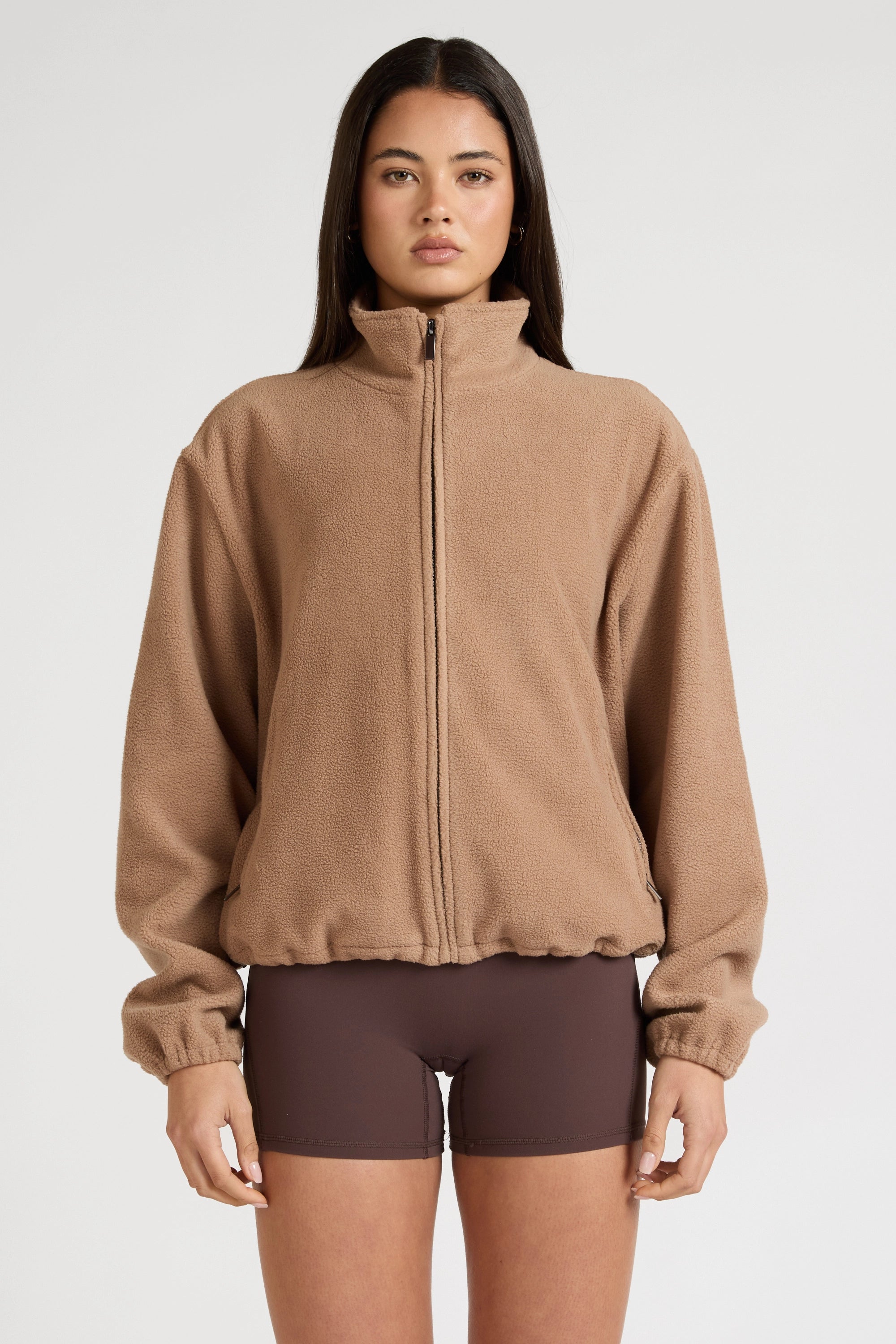 Woman wearing a brown fleece jacket and shorts on a white background