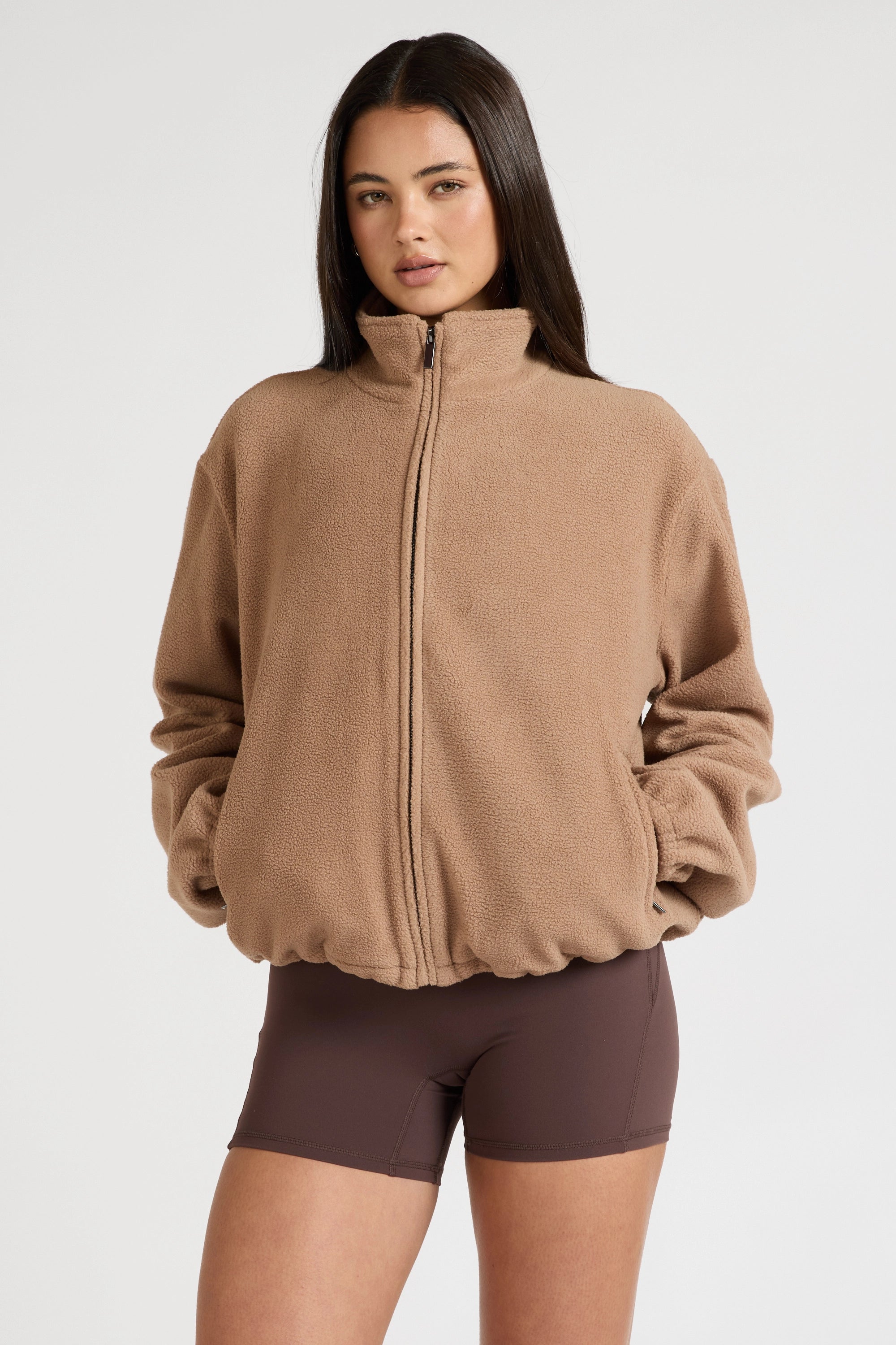Woman wearing a brown fleece jacket and shorts on a white background