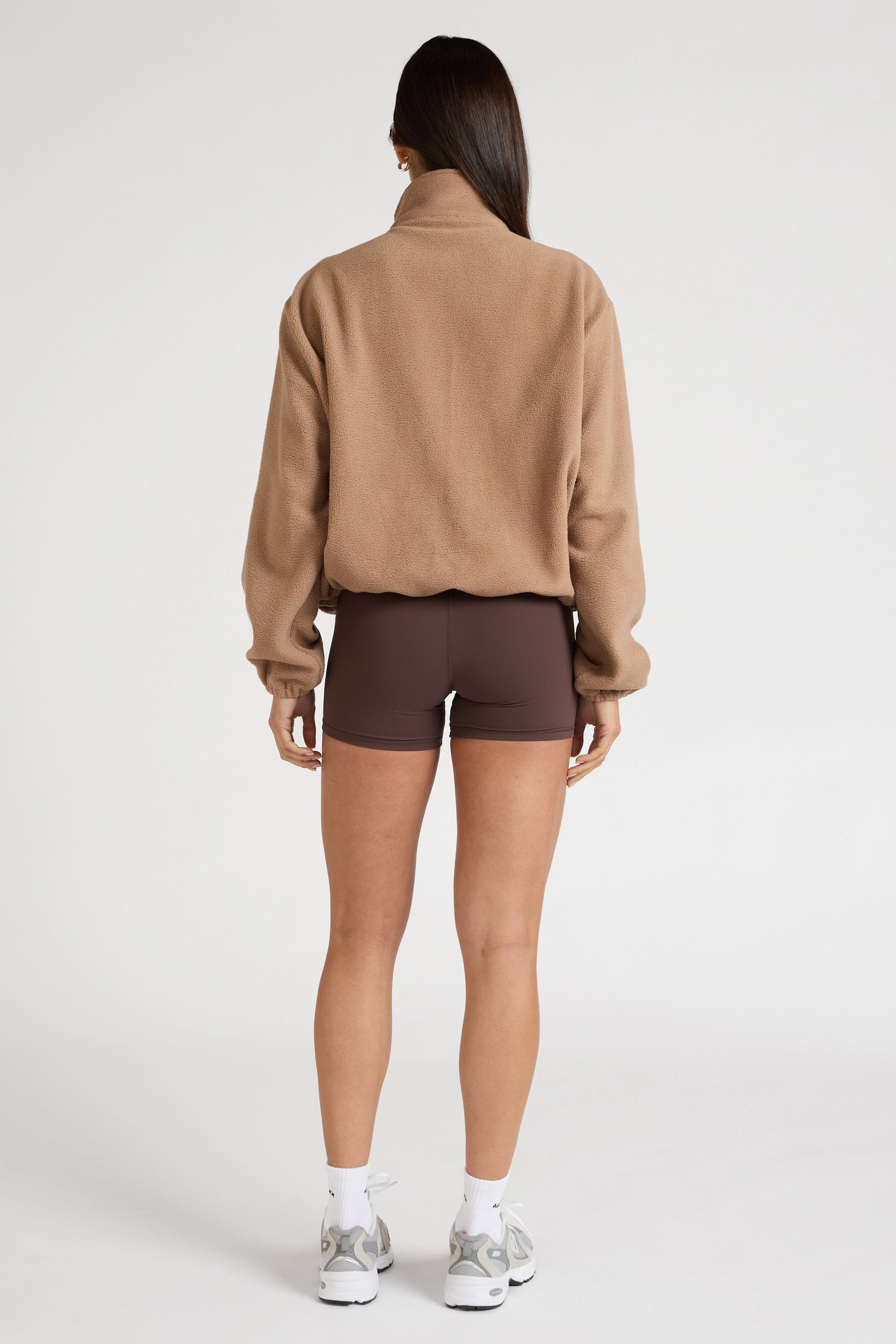 Woman wearing a brown soft fleece zip up jacket and brown shorts on a white background